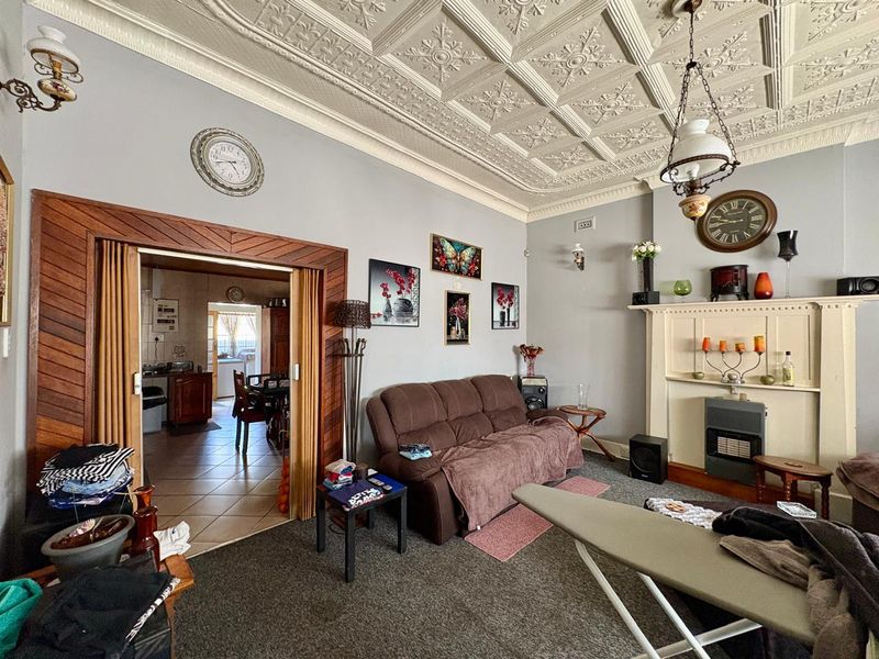 A living room featuring an ornate pressed metal ceiling, a fireplace mantel with a gas heater, and timber folding doors leading to the kitchen area.
