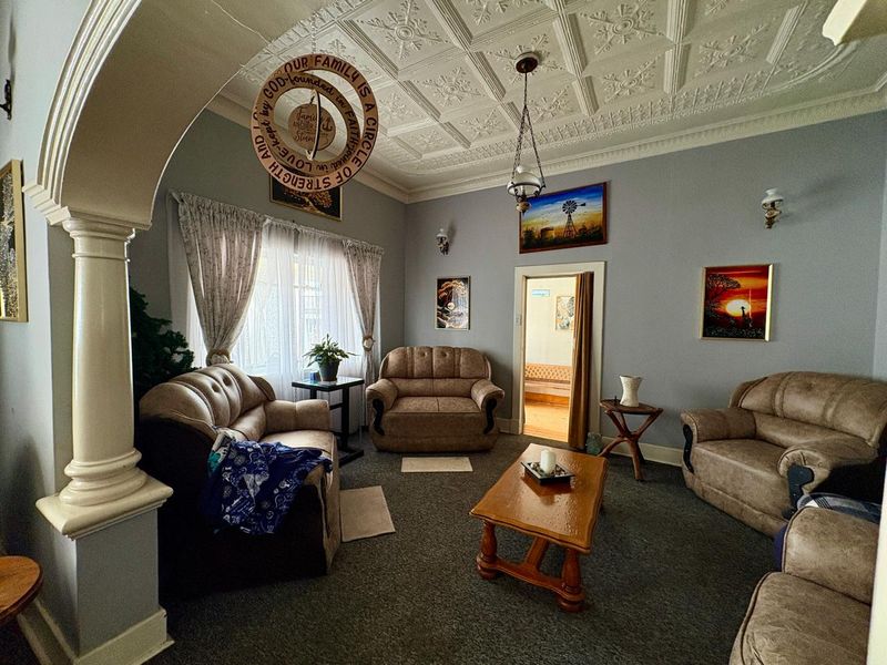 A living room featuring a classic decorative pressed metal ceiling, an elegant archway with a column, and wall sconce lighting.