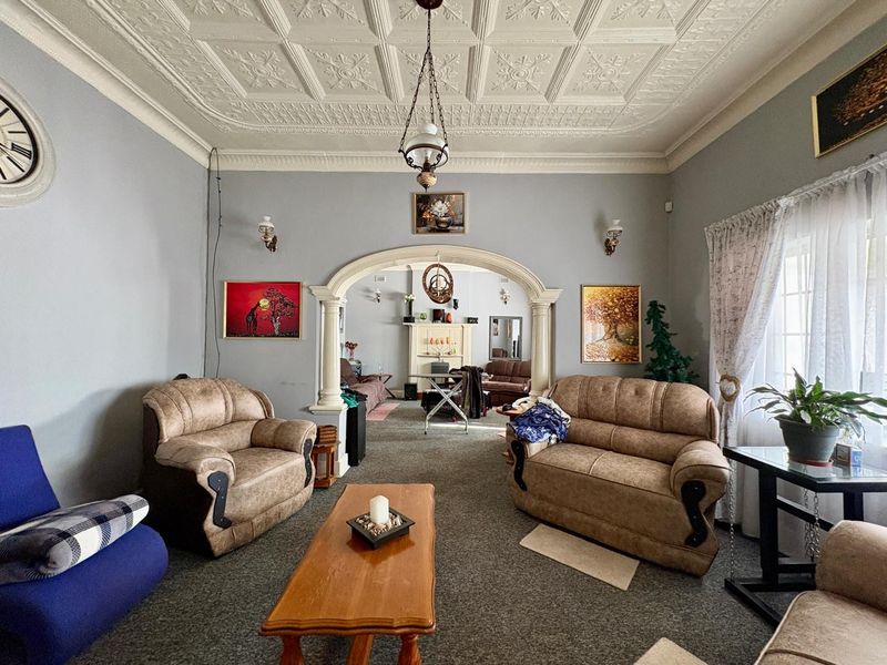 Spacious living room featuring a decorative pressed metal ceiling, classic archway with columns, and a fireplace mantel, offering a traditional character aesthetic.
