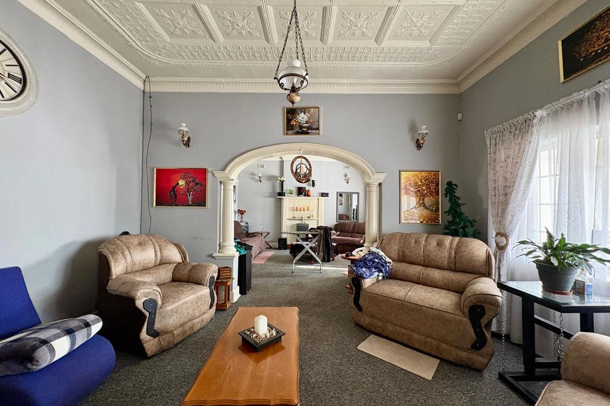 Spacious living room featuring a decorative pressed metal ceiling, classic archway with columns, and a fireplace mantel, offering a traditional character aesthetic.