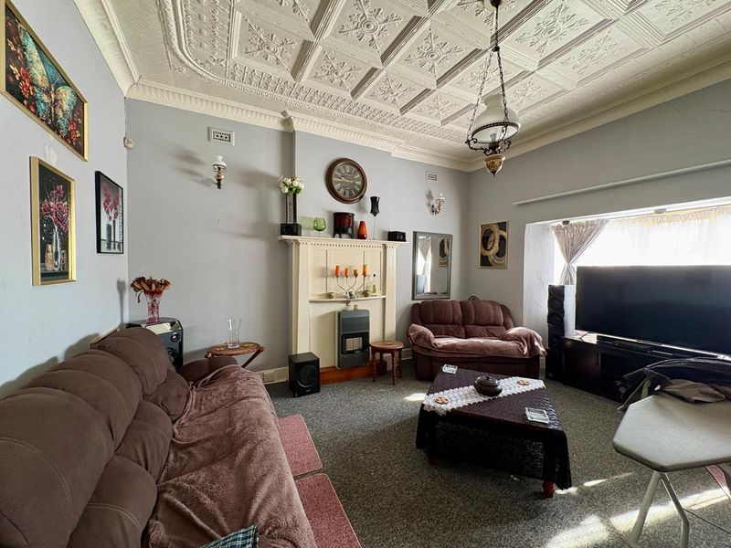 A living room featuring a traditional ornate pressed metal ceiling, fireplace mantel with gas heater, and wall sconces.