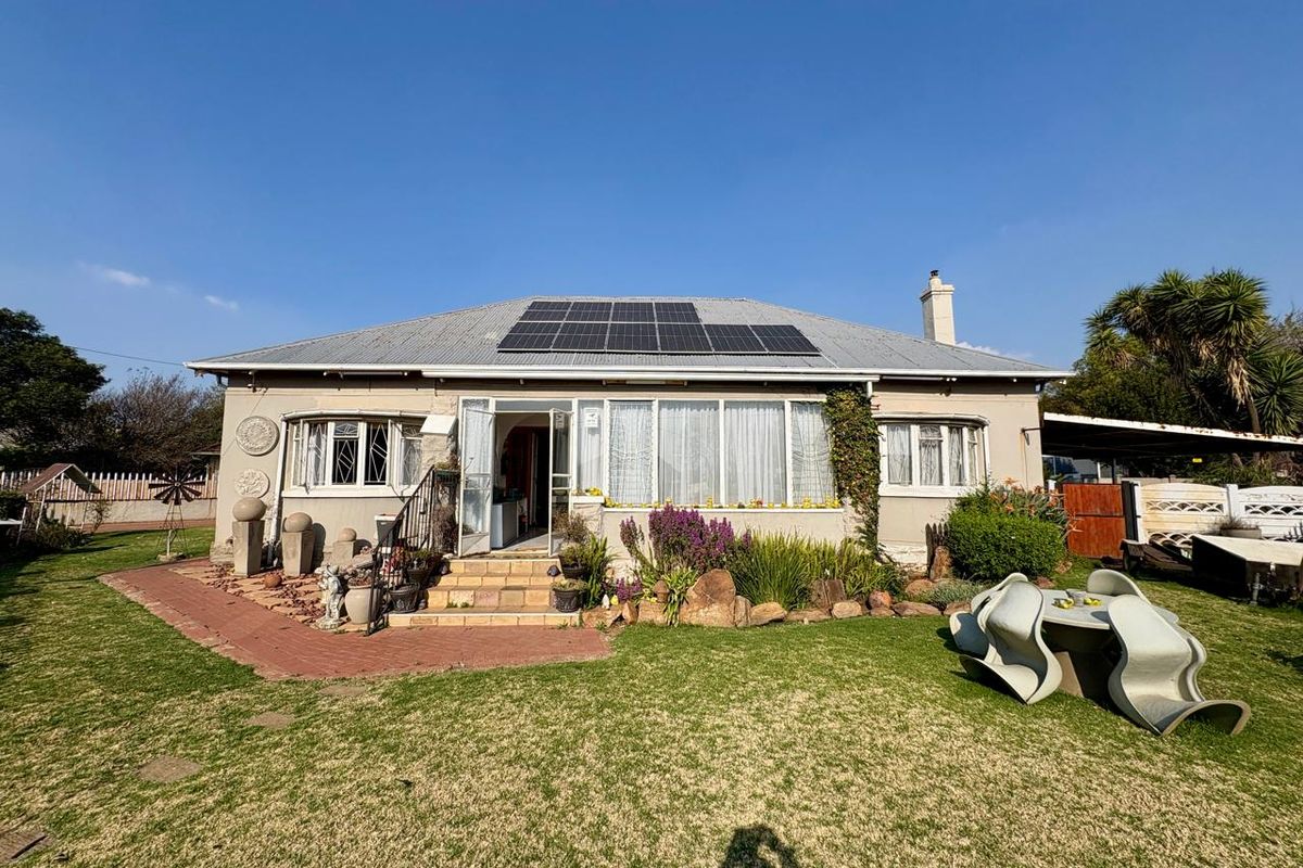 Rear view of a single-story house featuring a corrugated metal roof with installed solar panels, bay windows, and a well-maintained garden area.