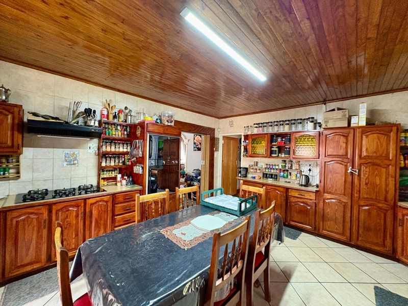 Spacious open-plan kitchen and dining area featuring extensive wooden cabinetry, built-in cooking appliances, tiled flooring, and a traditional wooden ceiling.