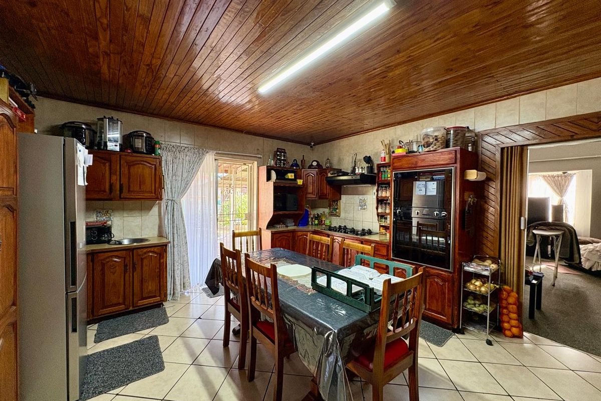 A traditional kitchen featuring wooden cabinetry, built-in oven, gas hob, and tiled flooring, with a warm wooden ceiling finish.