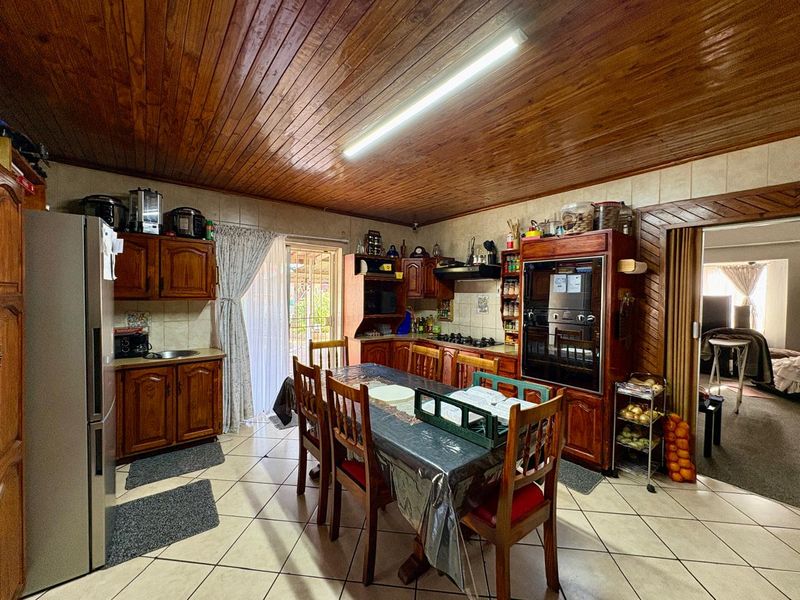 A traditional kitchen featuring wooden cabinetry, built-in oven, gas hob, and tiled flooring, with a warm wooden ceiling finish.