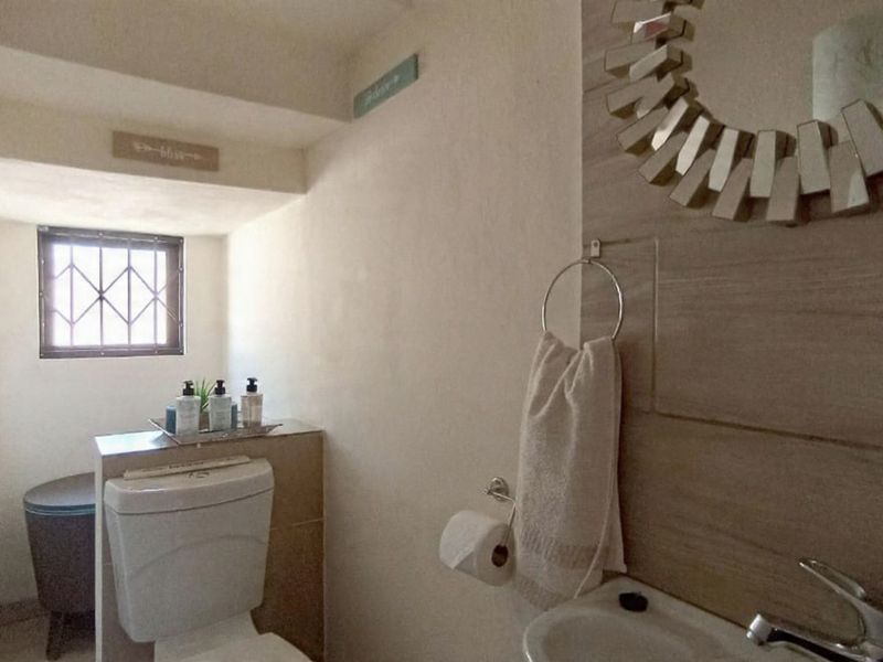 A compact bathroom featuring a toilet, basin with faucet, and decorative tiled wall cladding with security bars on the window.