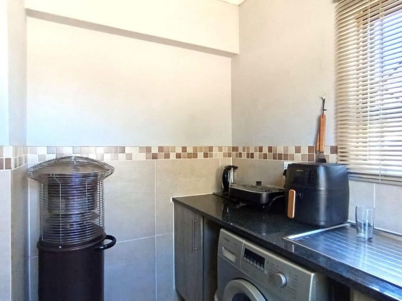 A functional laundry area featuring granite countertops, a stainless steel sink, tiled backsplash, and built-in cabinetry with venetian blinds.