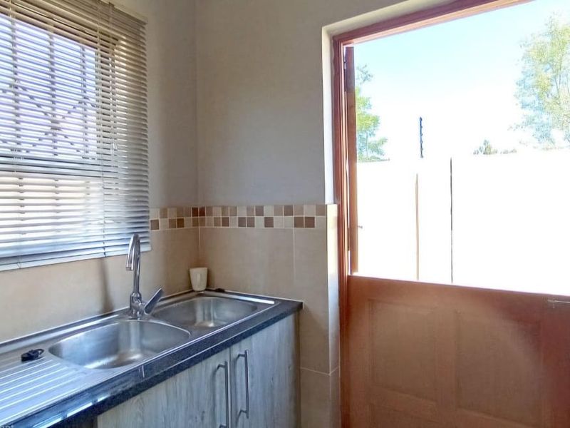 A functional scullery area featuring a double stainless steel sink, laminate cabinetry, tiled splashback, and a stable door leading to the exterior.
