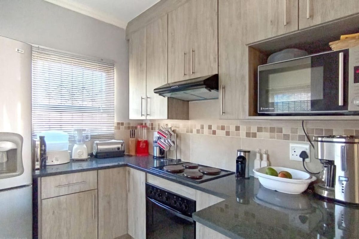 A functional kitchen featuring wood-look cabinetry, dark granite countertops, a built-in oven with hob, and a tiled backsplash.