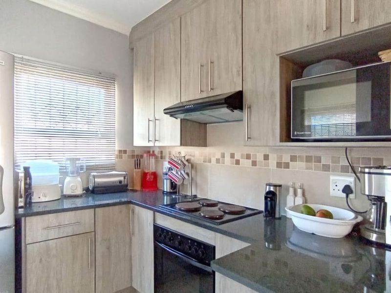 A functional kitchen featuring wood-look cabinetry, dark granite countertops, a built-in oven with hob, and a tiled backsplash.