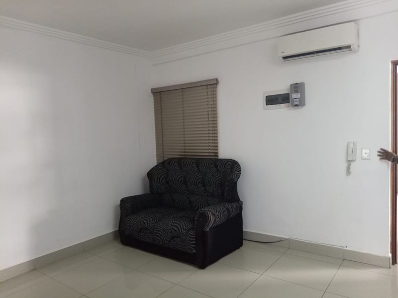 A living area featuring tiled flooring, a wall-mounted air conditioning unit, an intercom system, and venetian blinds.