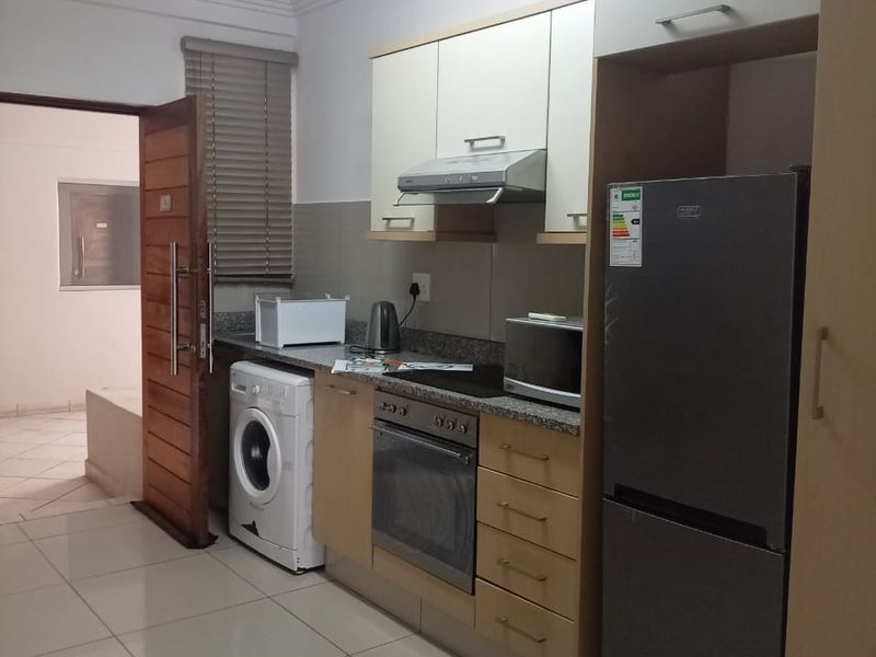 Compact kitchen featuring built-in cabinetry, granite countertops, integrated oven and hob, and tiled flooring with an adjacent laundry area.