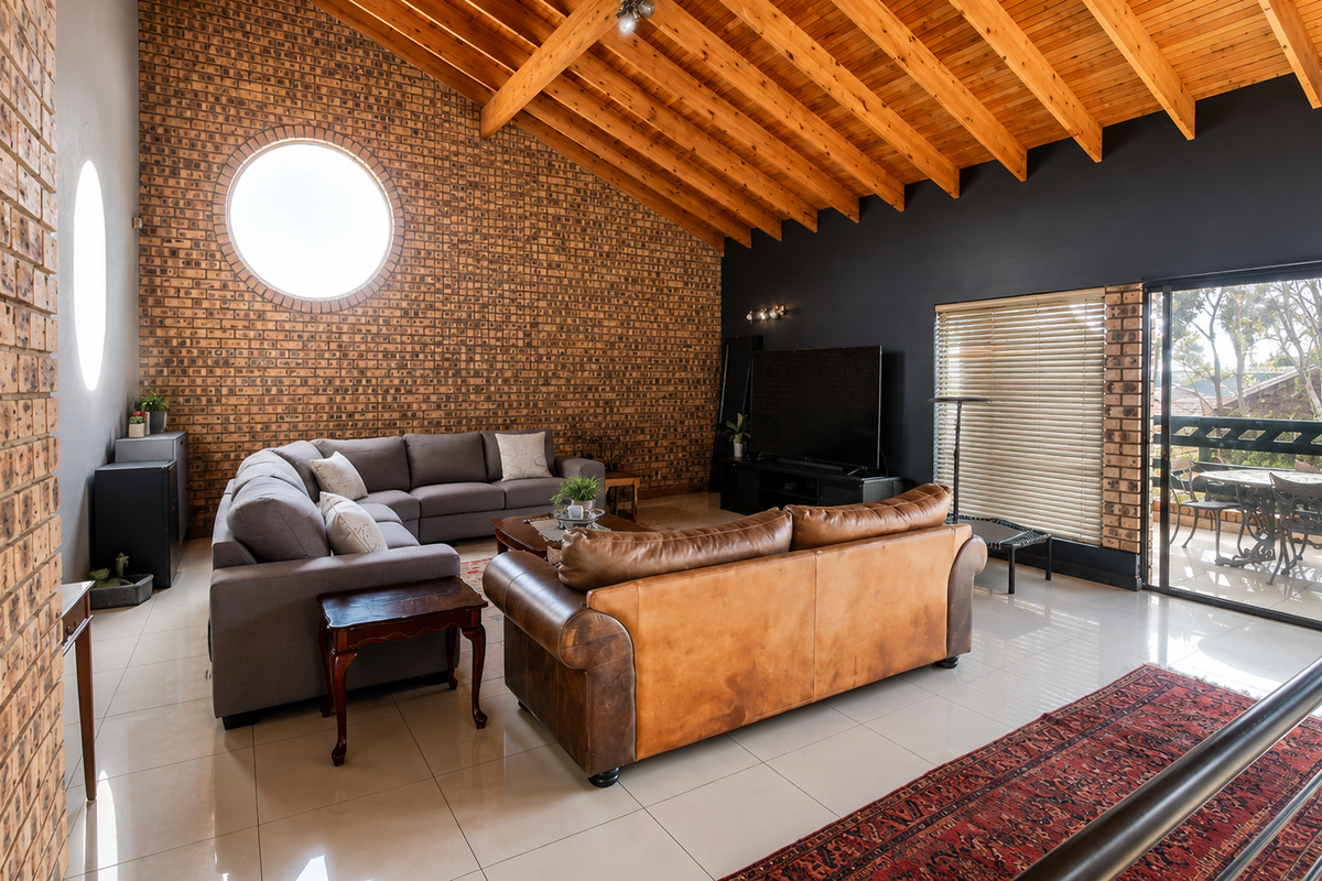 Spacious living room featuring a high vaulted timber ceiling, striking face brick feature wall with a circular window, and direct access to a balcony.