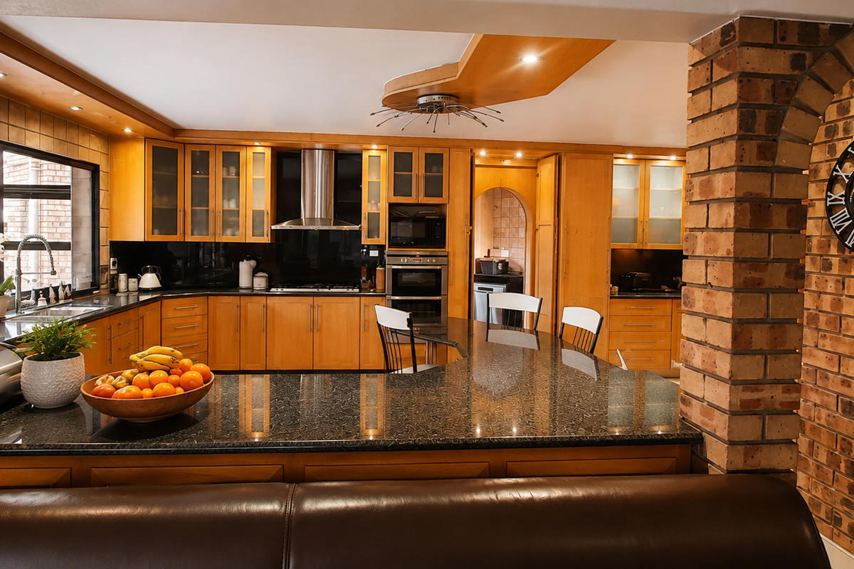 A well-appointed kitchen featuring warm wooden cabinetry, granite countertops, a built-in double oven, and a distinctive exposed brick archway.