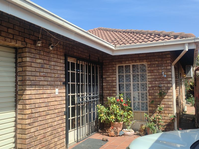 Front exterior view of a face brick house featuring a tiled roof, security gate, and a roller shutter garage door.