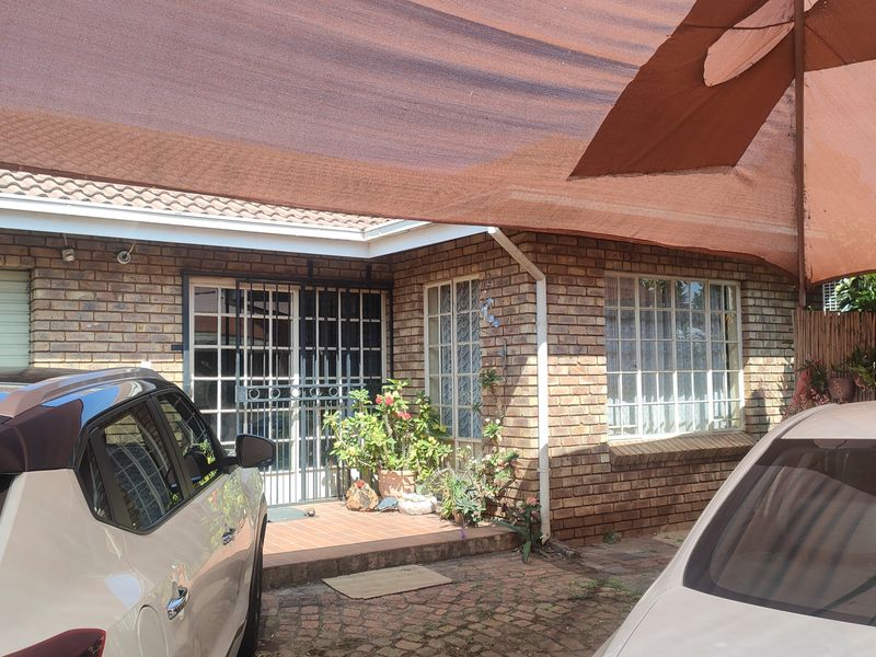 Front exterior view of a face brick house featuring a paved driveway, security gate, and a large shade sail covering the entrance area.