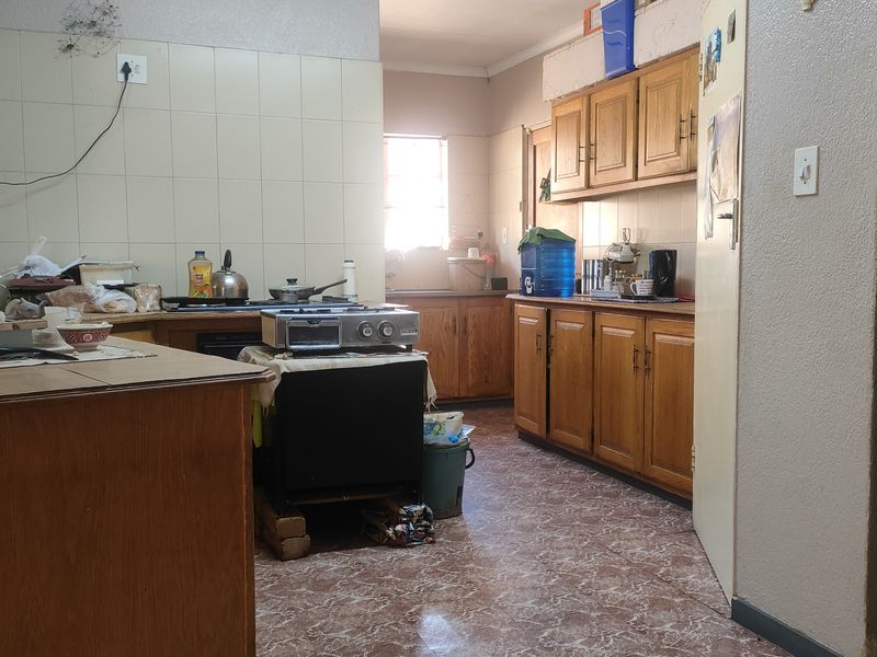 A dated kitchen featuring wooden cabinetry, tiled splashbacks, and tiled flooring, offering significant potential for a modern renovation and aesthetic update.