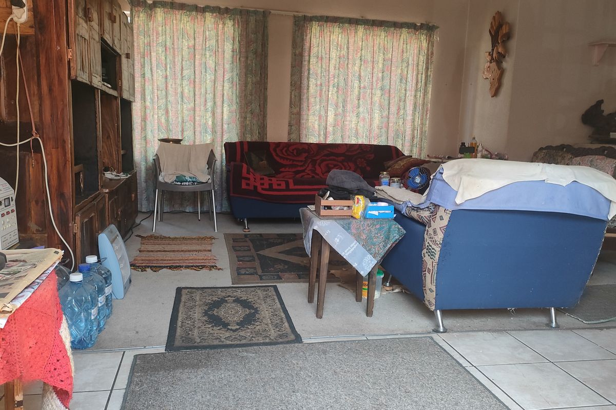 A living room area featuring tiled flooring and large windows with curtains, providing a functional space for relaxation.