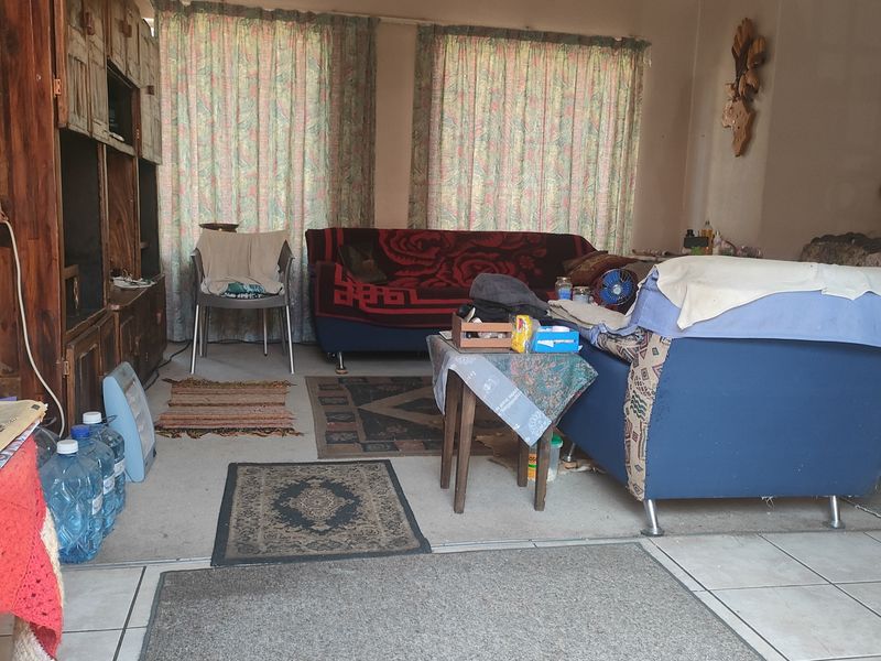A living room area featuring tiled flooring and large windows with curtains, providing a functional space for relaxation.