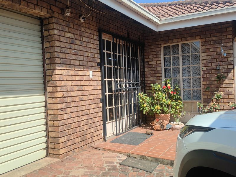 Front entrance area featuring a face brick facade, secure gated entry, tiled porch, and an integrated roller garage door.