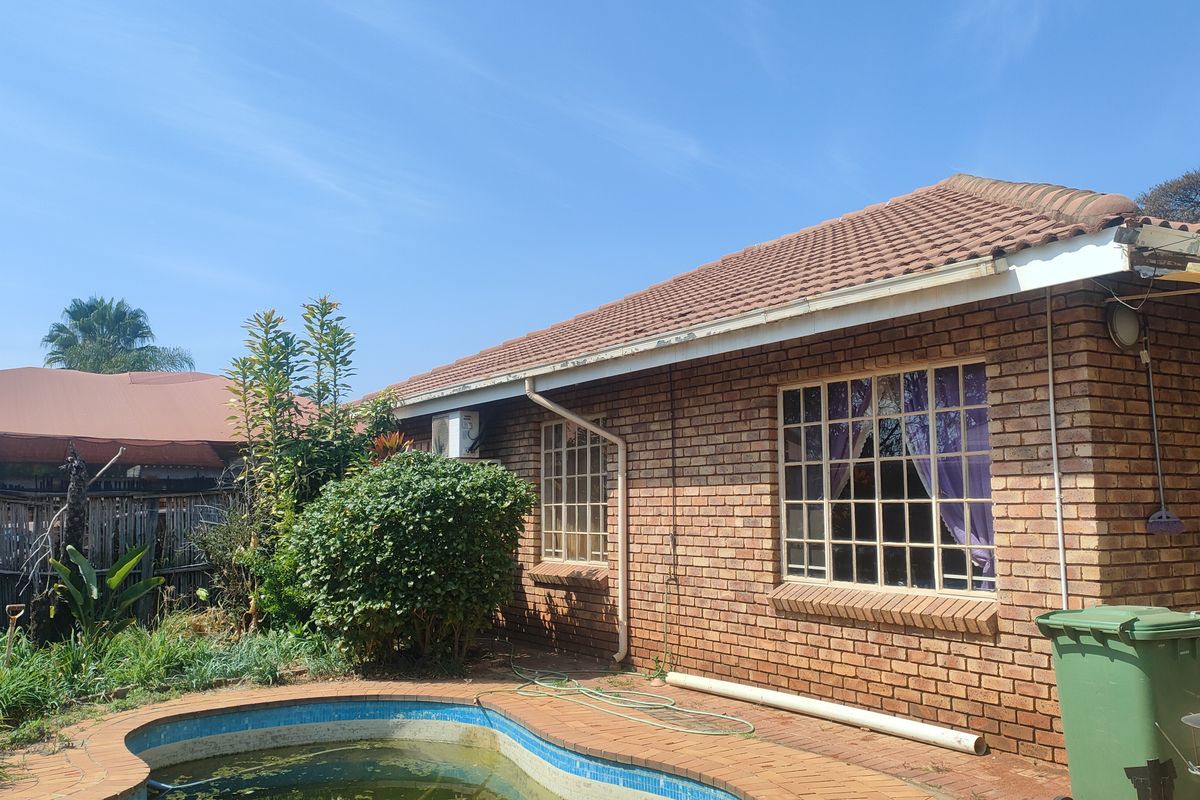 Rear exterior view of a brick house featuring a swimming pool, tiled roof, and security-barred windows.