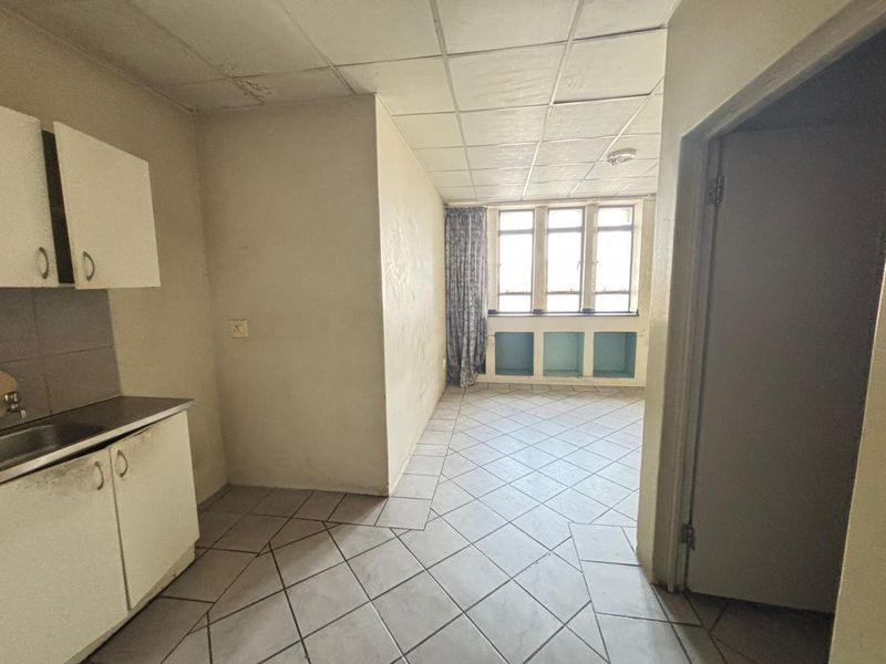 An empty kitchen area featuring tiled floors, built-in cabinetry with a sink, and a drop ceiling, requiring cosmetic updates and refurbishment.