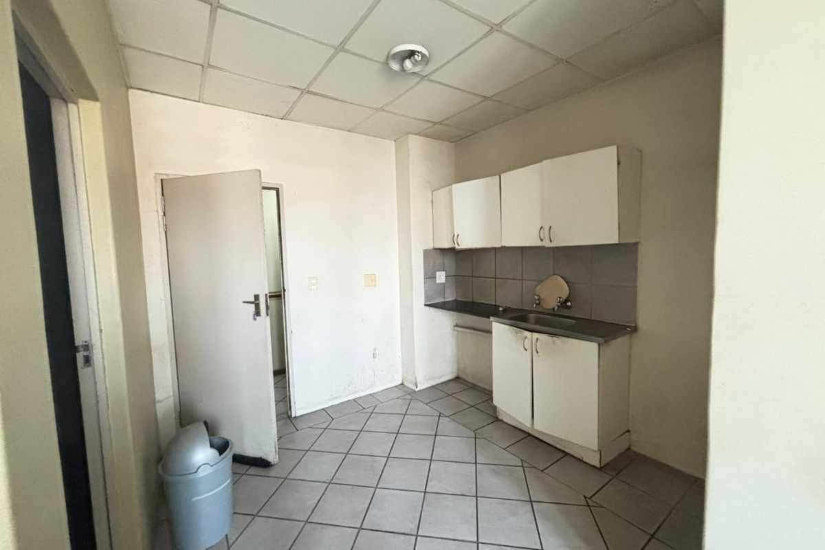 A compact kitchen featuring basic built-in cabinetry, a stainless steel sink, tiled backsplash, and tiled flooring, requiring cosmetic updates.