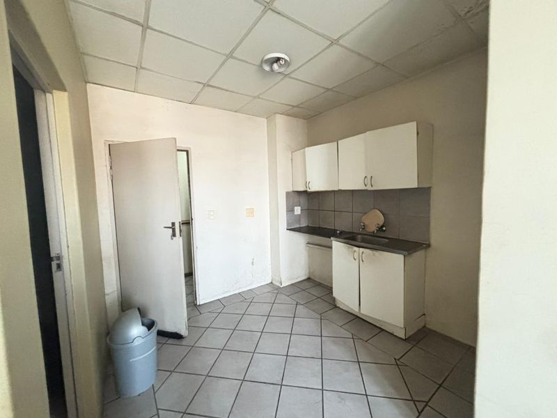 A compact kitchen featuring basic built-in cabinetry, a stainless steel sink, tiled backsplash, and tiled flooring, requiring cosmetic updates.