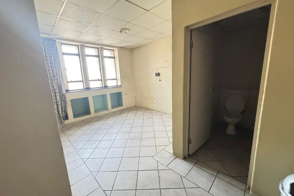 An empty bedroom featuring tiled flooring, a drop ceiling, built-in shelving, and an attached en-suite toilet, requiring cosmetic updates.