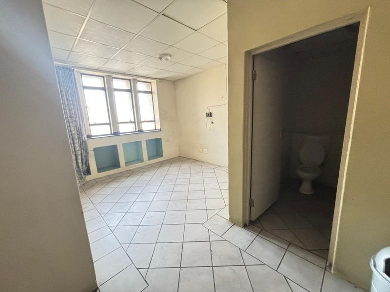 An empty bedroom featuring tiled flooring, a drop ceiling, built-in shelving, and an attached en-suite toilet, requiring cosmetic updates.
