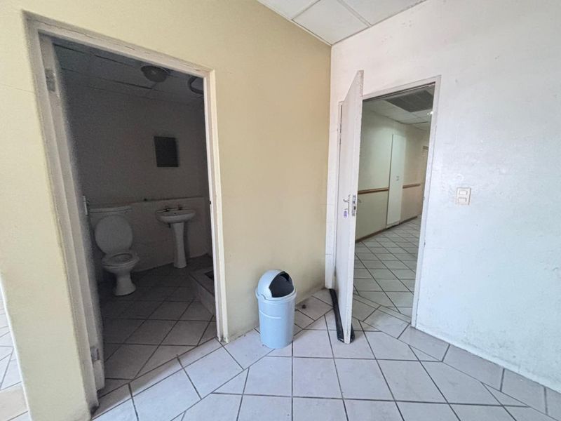 A vacant hallway area featuring tiled flooring and access to an adjacent bathroom, showing signs of wear and requiring cosmetic updates.