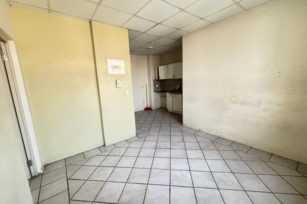 An empty open-plan living and kitchen area featuring tiled flooring and a drop ceiling, requiring cosmetic updates and wall repairs.