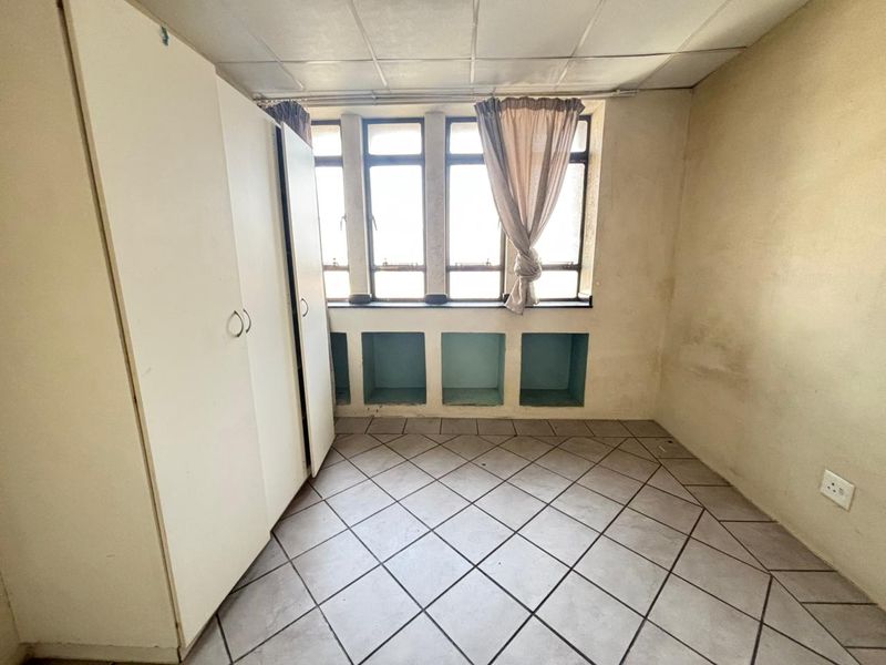 A bedroom featuring tiled flooring, built-in cupboards, and integrated shelving beneath the window, requiring cosmetic updates to the walls and ceiling.