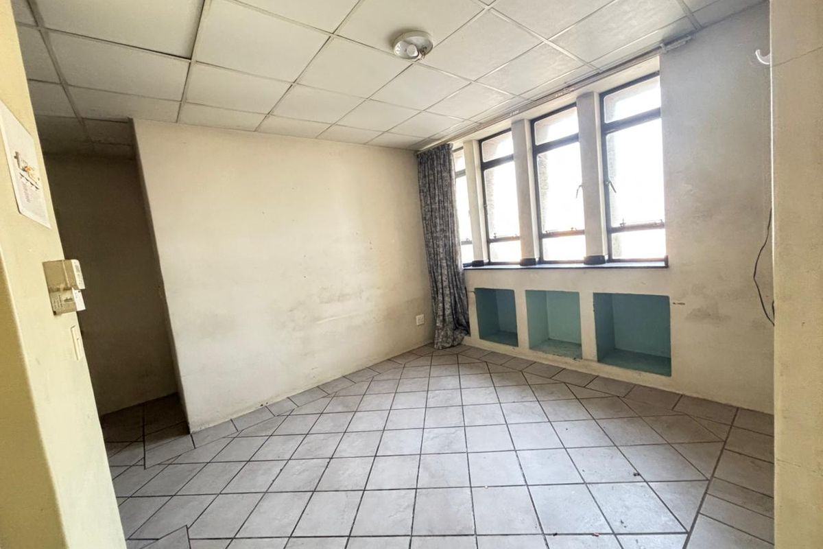 An empty living area featuring tiled flooring, a drop ceiling, and built-in wall niches under large windows, requiring cosmetic updates.