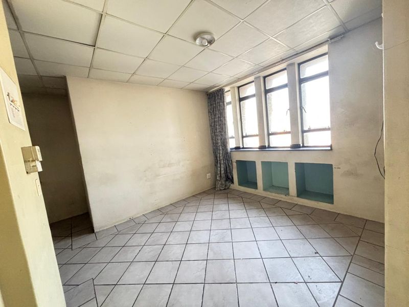 An empty living area featuring tiled flooring, a drop ceiling, and built-in wall niches under large windows, requiring cosmetic updates.