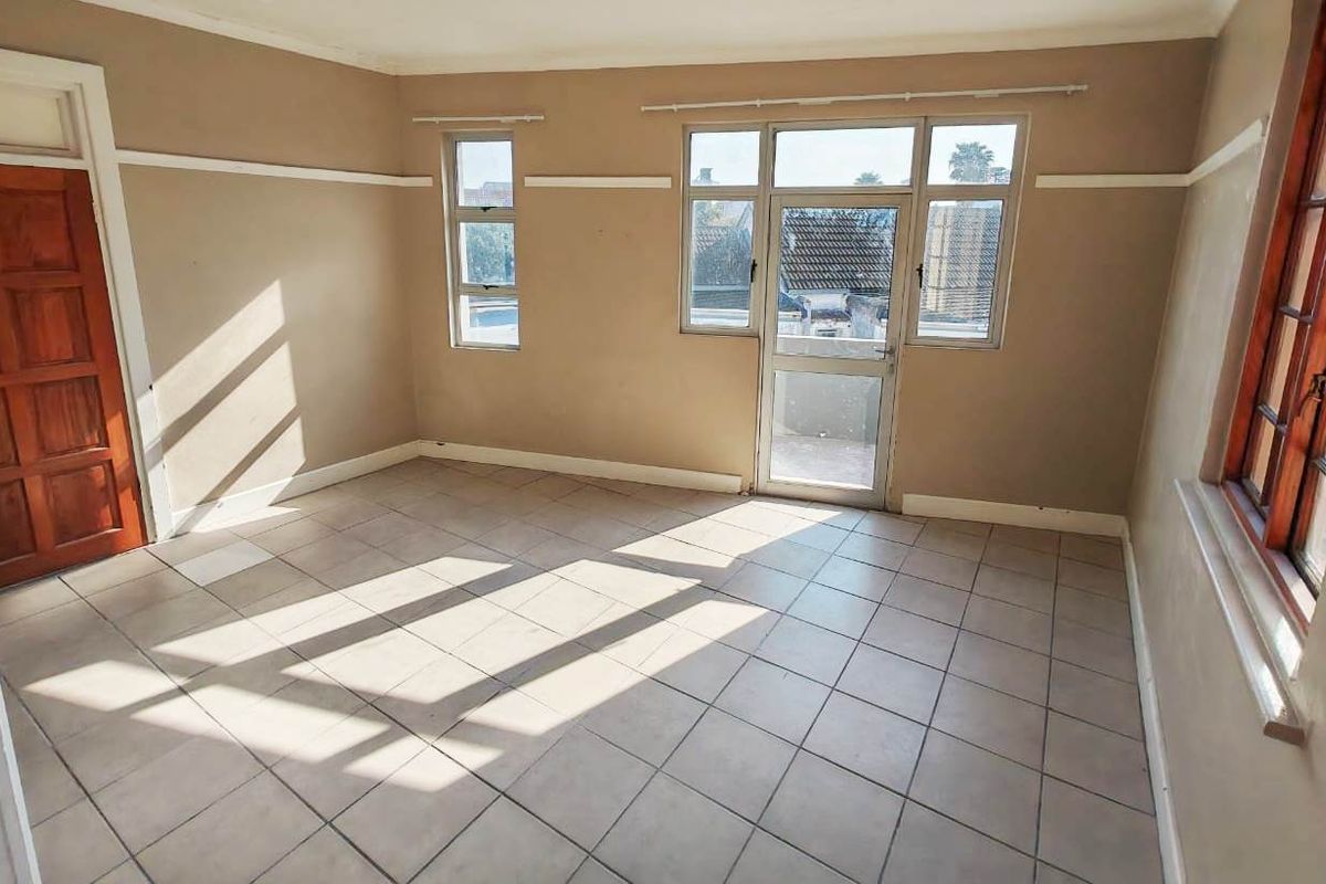 An empty living room featuring tiled flooring, neutral wall paint, and access to an outdoor balcony through a glass door.