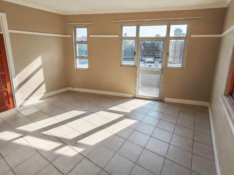 An empty living room featuring tiled flooring, neutral wall paint, and access to an outdoor balcony through a glass door.