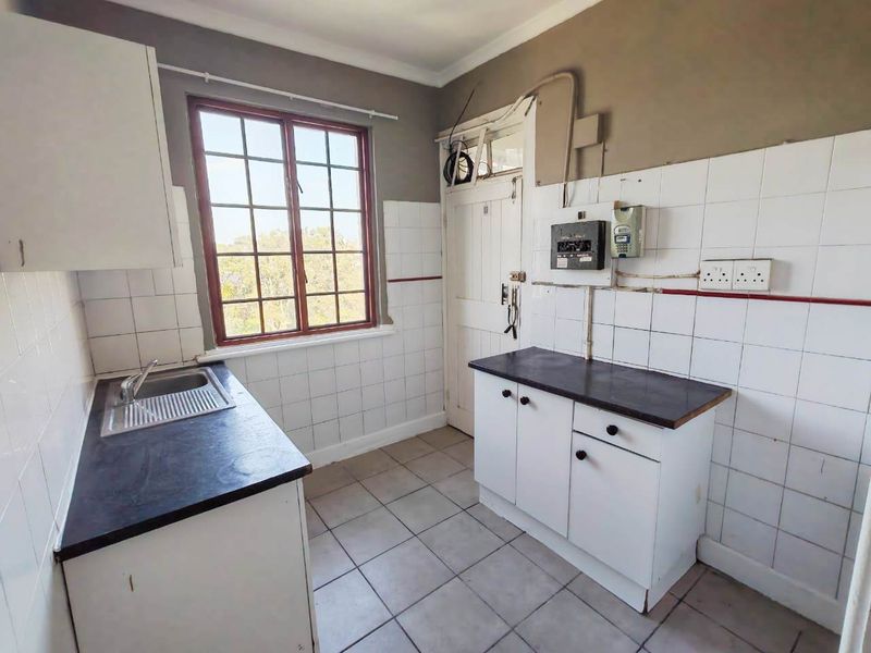A compact, dated kitchen featuring tiled splashbacks, laminate countertops, and a stainless steel sink, requiring cosmetic updates and electrical maintenance.