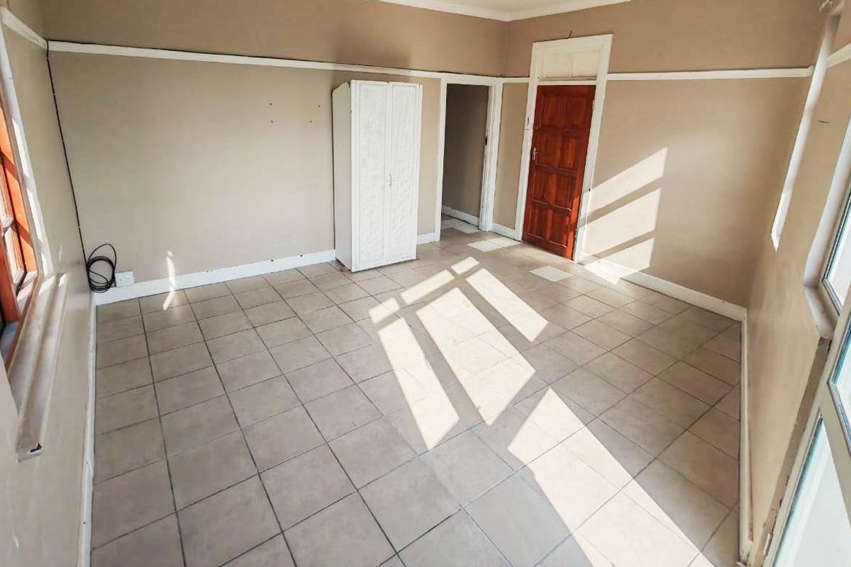 A vacant bedroom featuring tiled flooring, timber-framed windows, and neutral wall tones, offering a blank canvas for potential renovation or interior design updates.