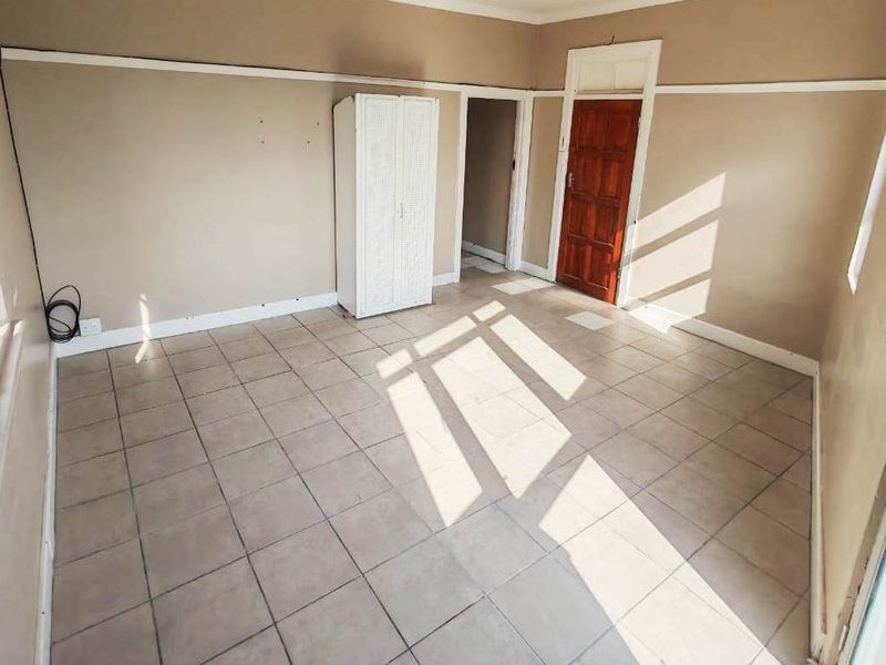 A vacant bedroom featuring tiled flooring, timber-framed windows, and neutral wall tones, offering a blank canvas for potential renovation or interior design updates.