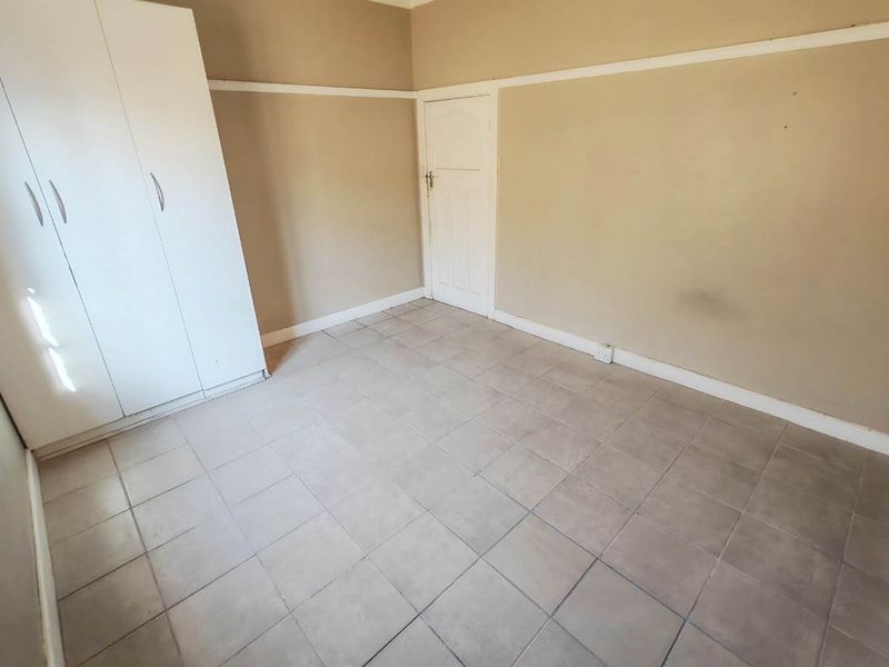 An empty bedroom featuring tiled flooring, a built-in wardrobe, and neutral wall finishes with a classic picture rail.
