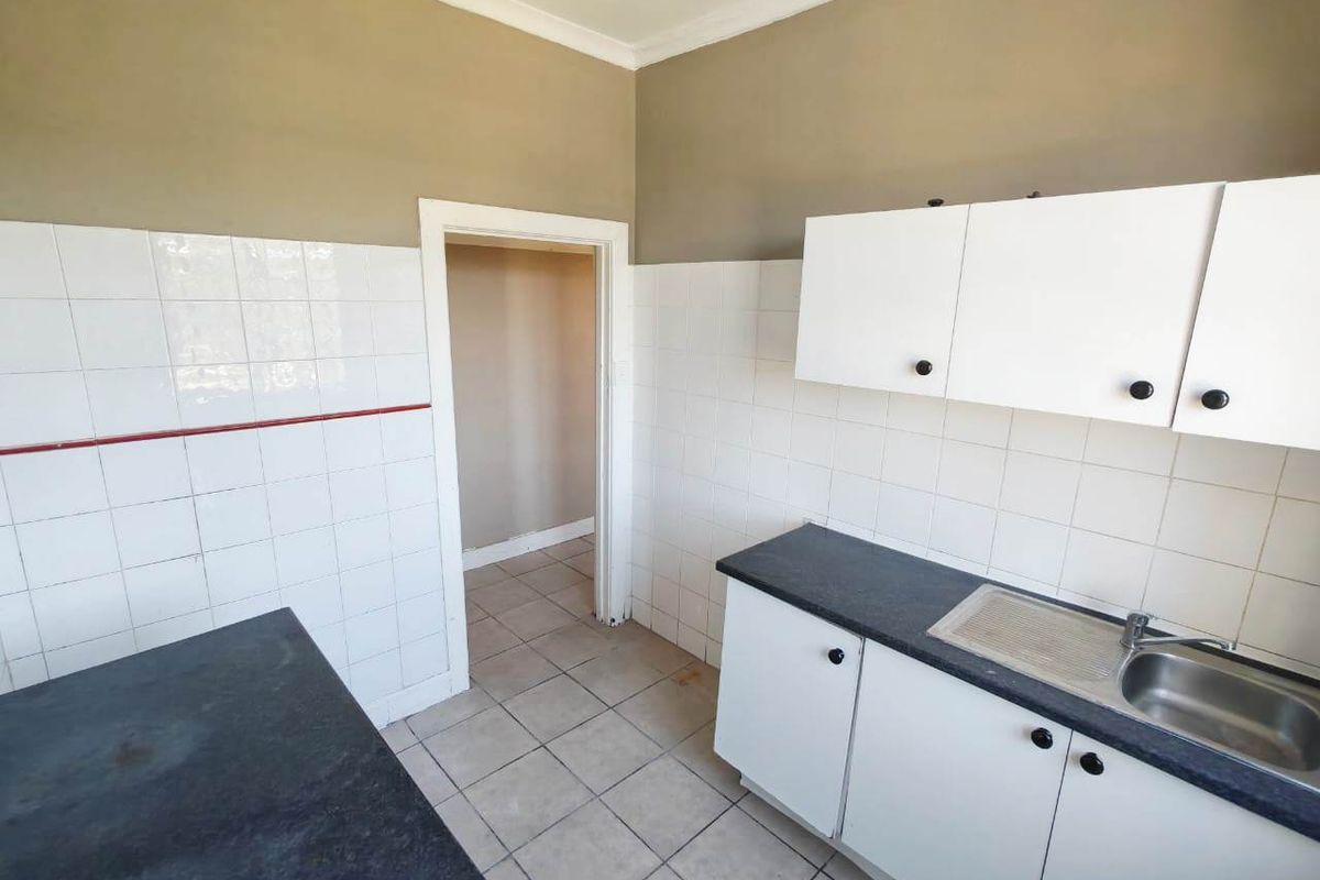 A functional kitchen space featuring white cabinetry, dark laminate countertops, stainless steel sink, and tiled finishes, ready for a modern update.