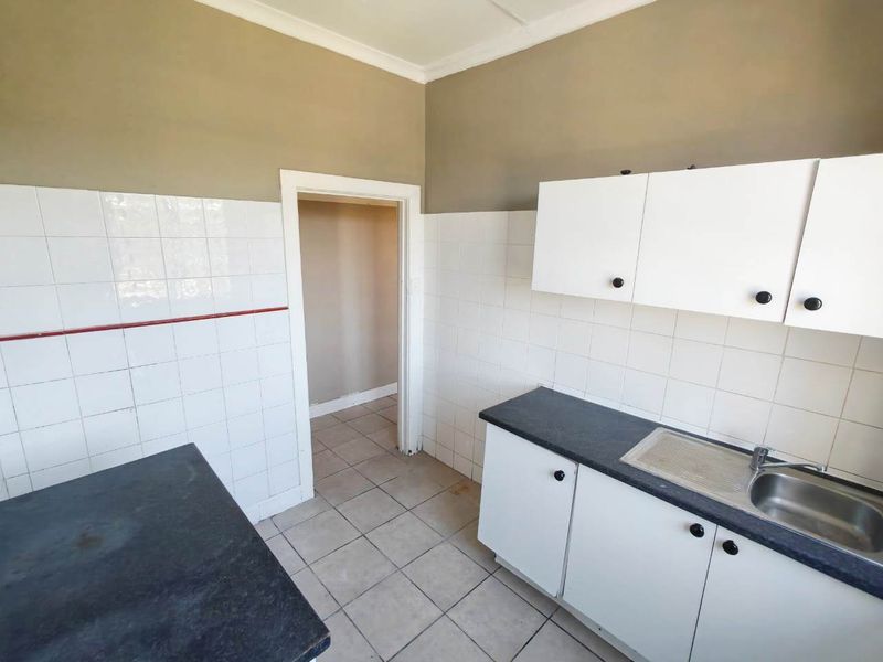 A functional kitchen space featuring white cabinetry, dark laminate countertops, stainless steel sink, and tiled finishes, ready for a modern update.