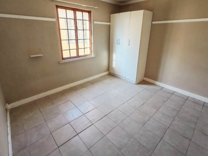 A vacant bedroom featuring tiled flooring, a built-in wardrobe, and a wooden window frame, offering a blank canvas for potential updates.