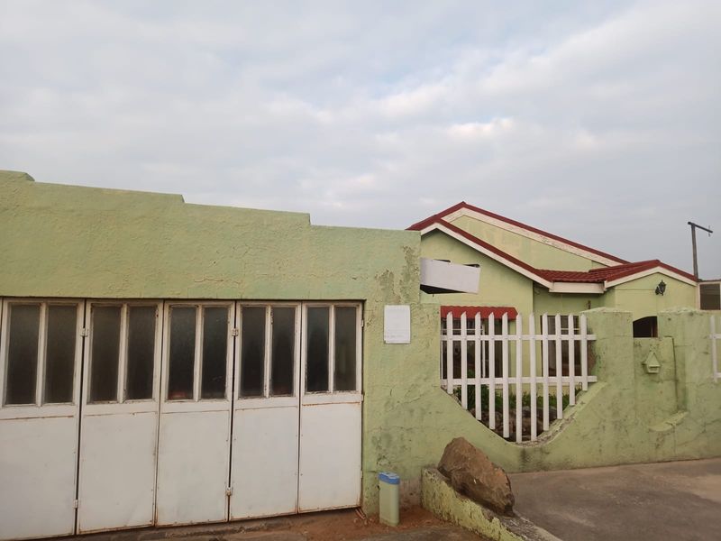 Front exterior view of the house featuring a metal garage door, perimeter wall with picket fencing, and a tiled roof structure.