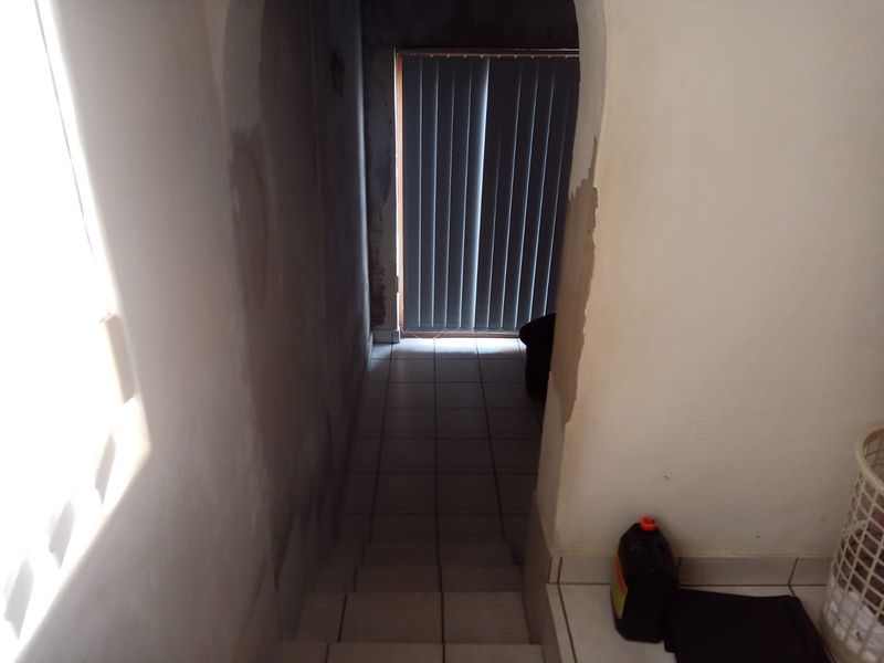 A narrow hallway featuring tiled flooring and an arched entryway, currently requiring wall finishing and plastering to complete the space.