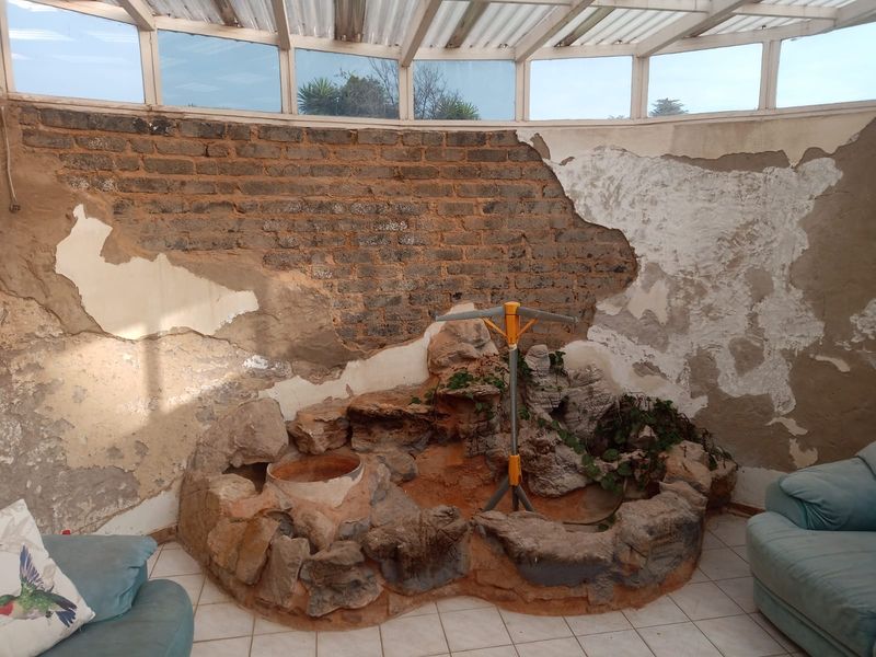 Enclosed patio area featuring a built-in rock feature and translucent roof, currently requiring significant wall plaster repairs and cosmetic restoration.