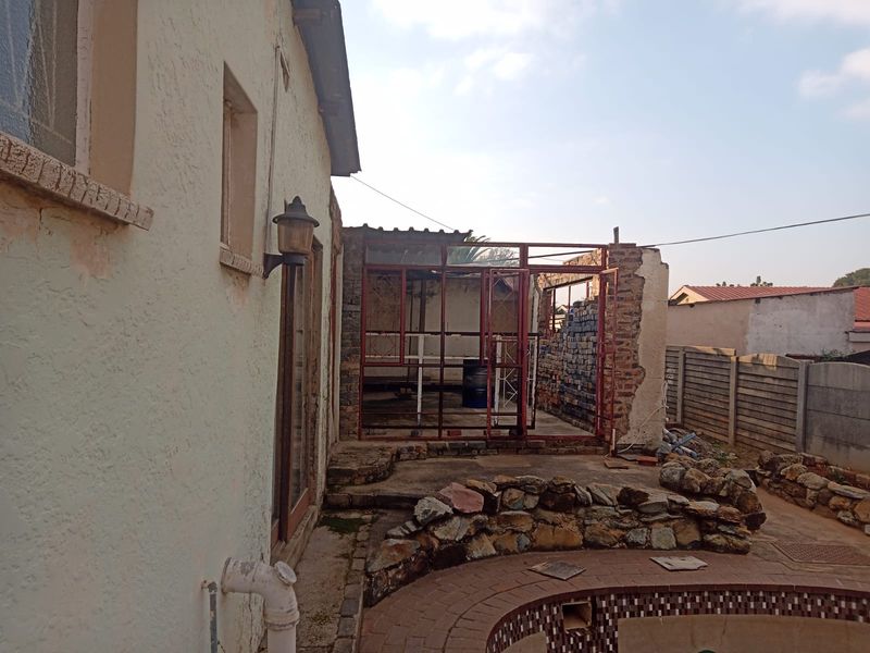 Rear exterior view showing a swimming pool and an unfinished, partially demolished structure with exposed brickwork and metal framing.