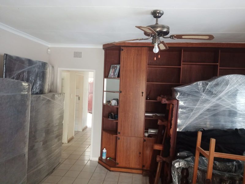 Living area featuring a large built-in wooden shelving unit, ceiling fan, and tiled flooring, currently used for storage.