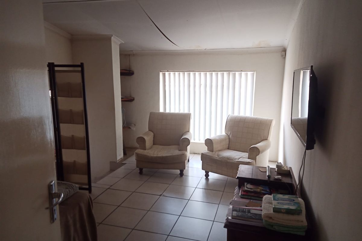 A living room featuring tiled flooring and vertical blinds, currently showing signs of ceiling damage and wear.